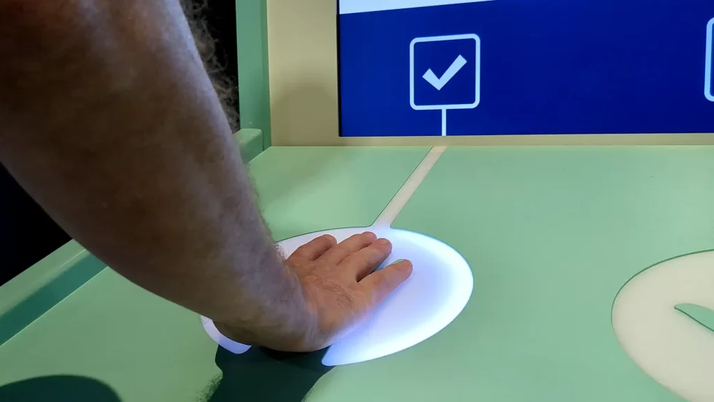 A hand activating a illuminated sensor on the Impact Station Interactive at Inside the Walls Exhibition